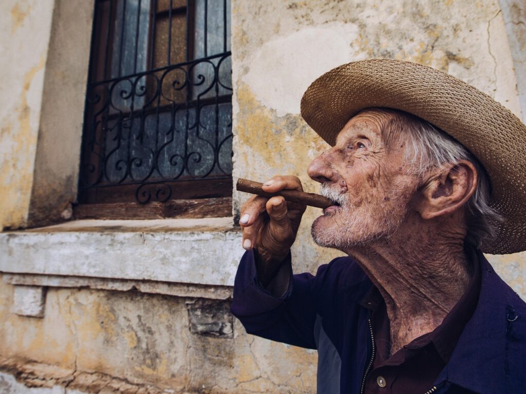 Hombre mayor con sombrero de paja fumando un puro en la calle